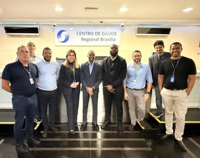 A group of nine people posing for a photo in front of the "Brasília Regional Data Center" sign during a visit by a delegation from Angola