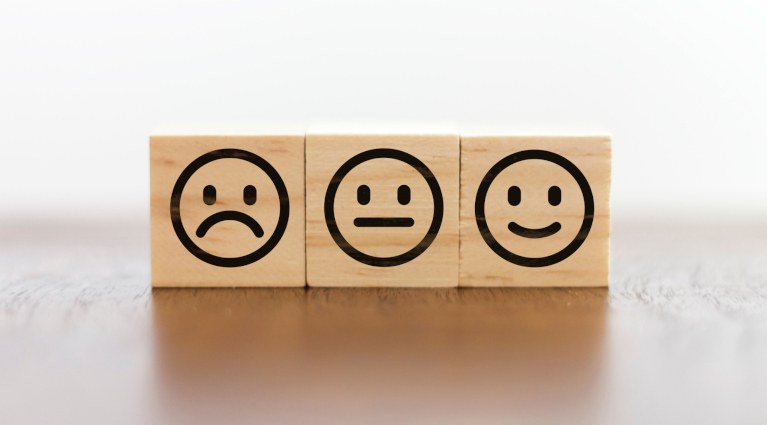 Foto com três cubos de madeiras com "carinhas" de triste, imparcial e feliz, representando a reputação de uma empresa perante seus clientes 