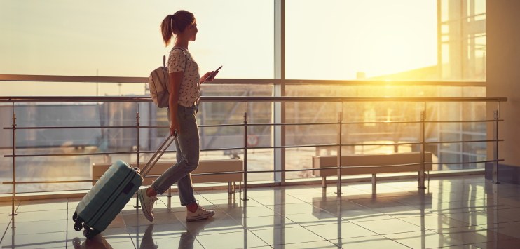 Mulher caminha em saguão do aeroporto com seu telefone celular em mãos