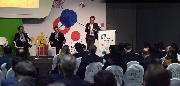 Foto do painel "Cases de Transformação Digital nos bancos brasileiros", apresentado no primeiro dia do Ciab Febraban com palestrantes da Caixa, e Itaú Unibanco. Na imagem, parte da plateia aparece de costas.