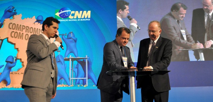 Diretor do Serpro, André de Cesero, assina acordo de cooperação com Paulo Ziulkoski, presidente da CNM, ao seu lado direito. Apresentador do evento está à esquerda, falando ao microfone