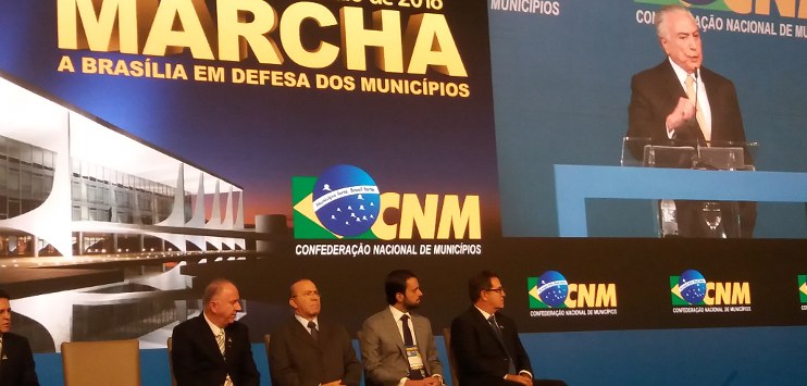 À direita, tela exibe imagem do presidente Temer falando. À esquerda, mais abaixo, quatro ministros estão sentados.