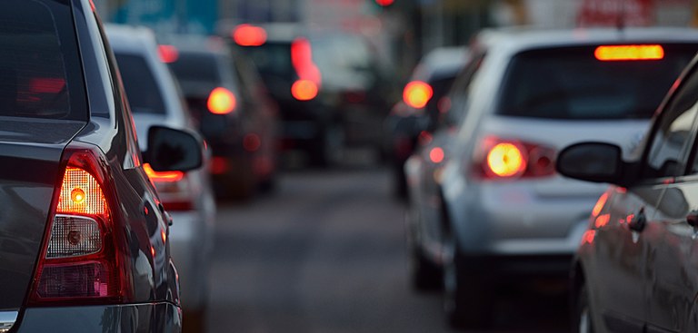 Numa rua de cidade brasileira, duas linhas de carros vistos de trás