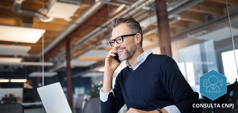 Homem em sua mesa de trabalho utilizando o celular e o computador