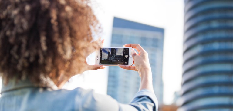 Mulher usa smartphone para tirar foto de prédios altos e espelhados Mulher usa smartphone para tirar foto de prédios altos e espelhados