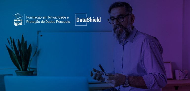 Fotografia de um professor interagindo com alunos por meio de um computador. Acima e à esquerda, marcas do Serpro LGPD e Datashield