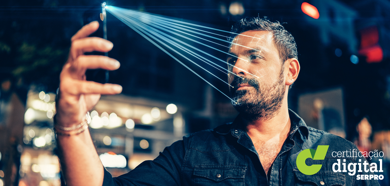 Foto de homem usando telefone celular para reconhecimento facial. Na posição de selfie, o celular emite luzes que mapeiam o rosto dele. No canto inferior direito, a marca: Certificação Digital Serpro.