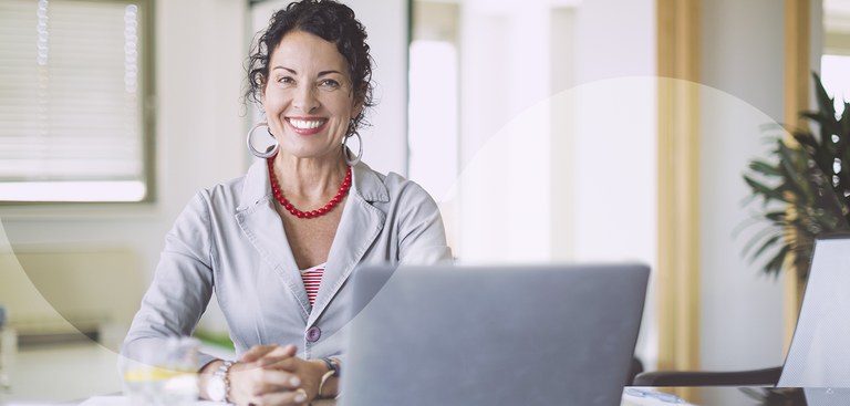 Mulher sorrindo com as mãos apoiadas em uma mesa onde está posicionado um laptop