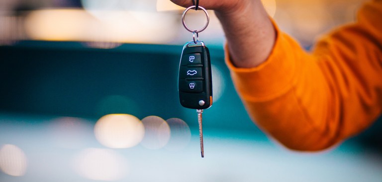 braço de homem de camisa laranja segurando uma chave de carro