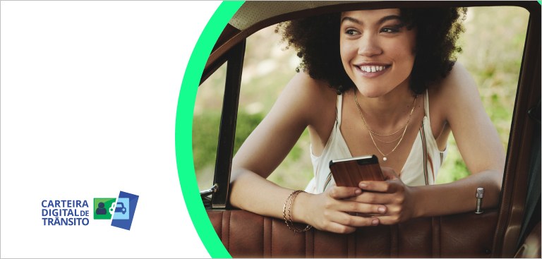 Apoiada na janela de um carro, mulher sorri com um celular nas mãos. À esquerda, aplicação da marca do app Carteira Nacional de Trânsito (CDT)