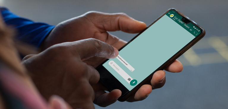Close das mãos de uma pessoa segurando um celular e acionando o Whatsapp da Certificação Digital do Serpro