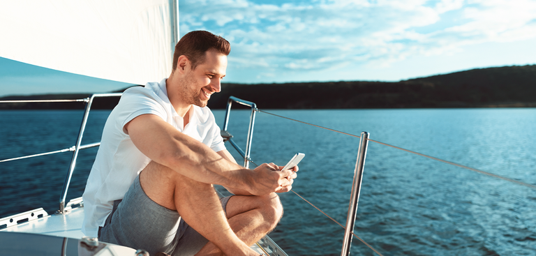 Homem acessando o celular sentado na proa de um barco