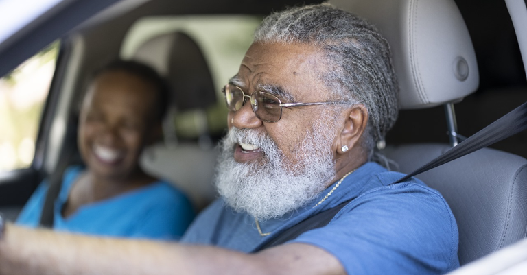 Homem idoso negro dirige carro com mulher idosa negra no carona.png