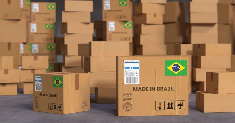 Caixas de papelão empilhadas em um galpão. Nelas pode-se ver a mensagem "made in Brazil" e a bandeira do Brasil, fazendo alusão a produtos brasileiros voltados à exportação