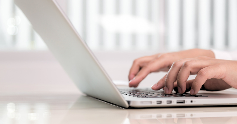 Foto de detalhe de mãos operando um teclado de computador