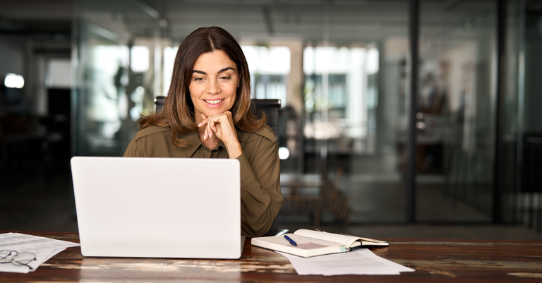 Fotografia de uma mulher trabalhando em um computador e sorrindo