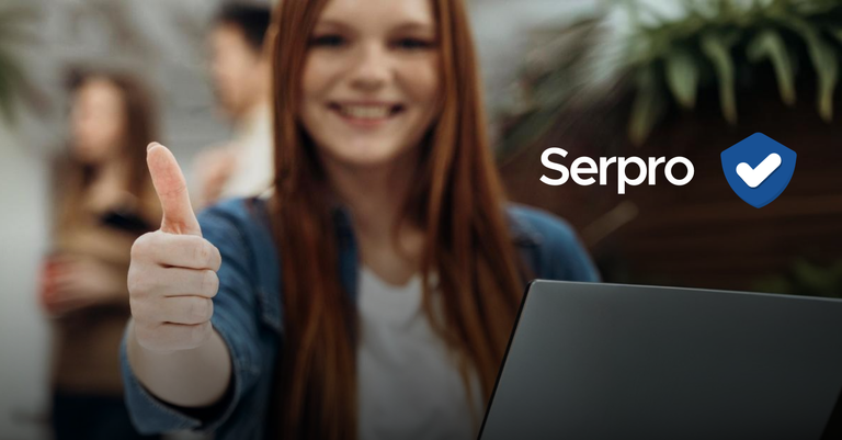 Mulher em frente a notebook faz o gesto de positivo com a mão, ao lado, o nome Serpro e o selo de verificado do Reclame AquiReclame Aqui Selo Serpro verificado