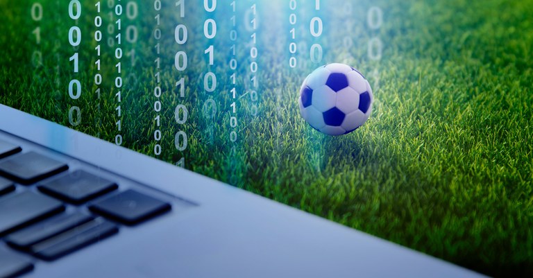 Teclado de notebook tendo ao lado um gramado verde e uma bola de futebol e zeros e uns pela imagem.jpeg